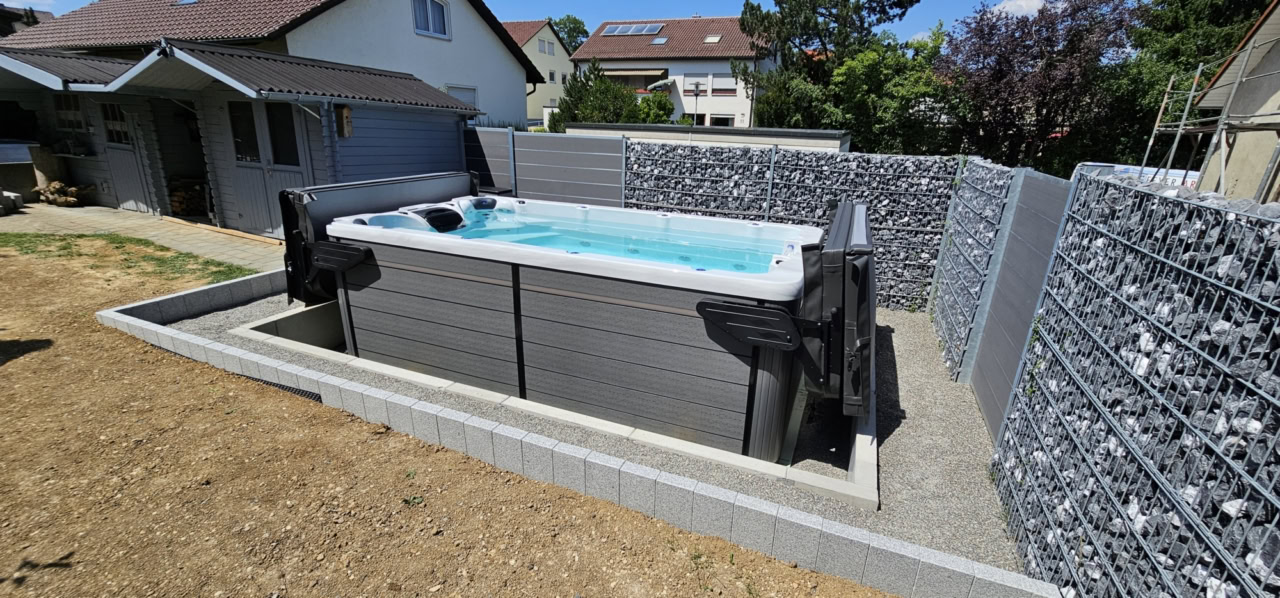 Zwei senkrecht geöffnete Premium II Abdeckungslifter hinter dem teilversenkten Swim Spa